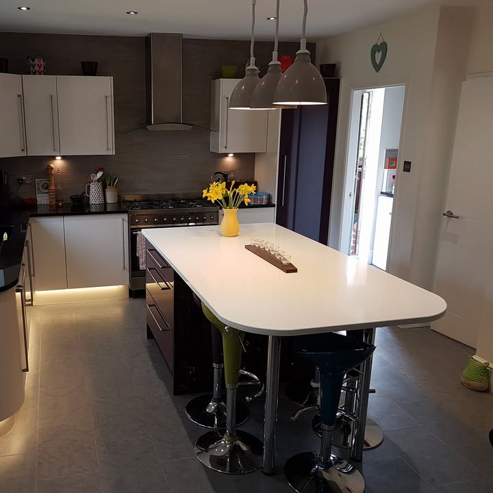 A fitted kitchen with white gloss units, an island breakfast bar and plinth lighting