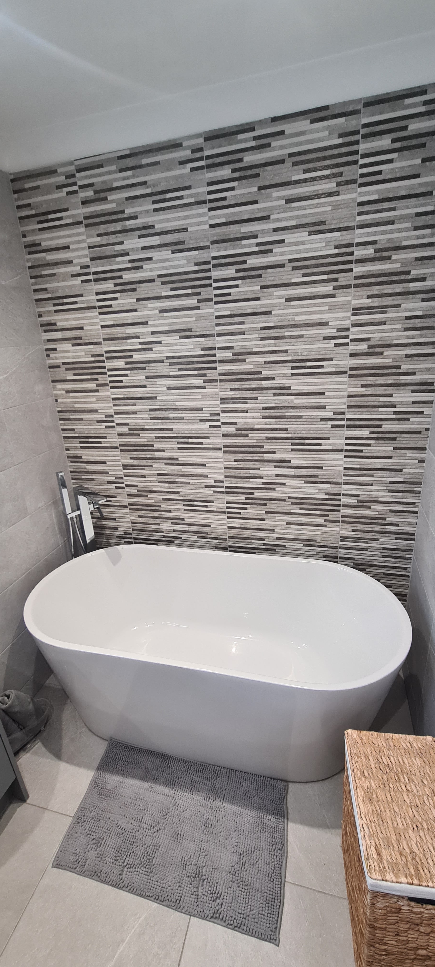 A finished bathroom with a freestanding bath against a grey mosaic feature wall