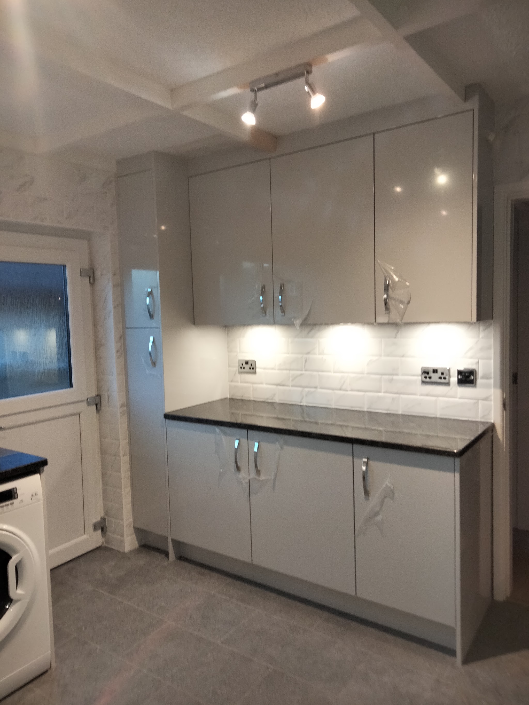 A newly fitted kitchen with grey gloss units, spotlights and a window over the worktop