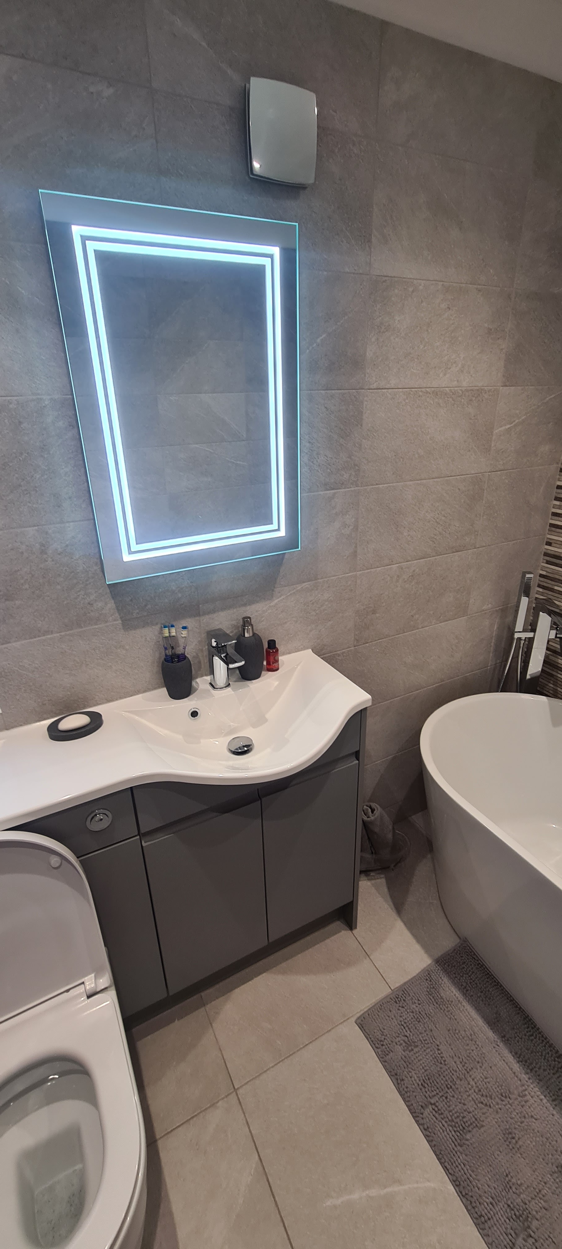 A bathroom with an LED lit mirror, a curved vanity unit and a freestanding bath