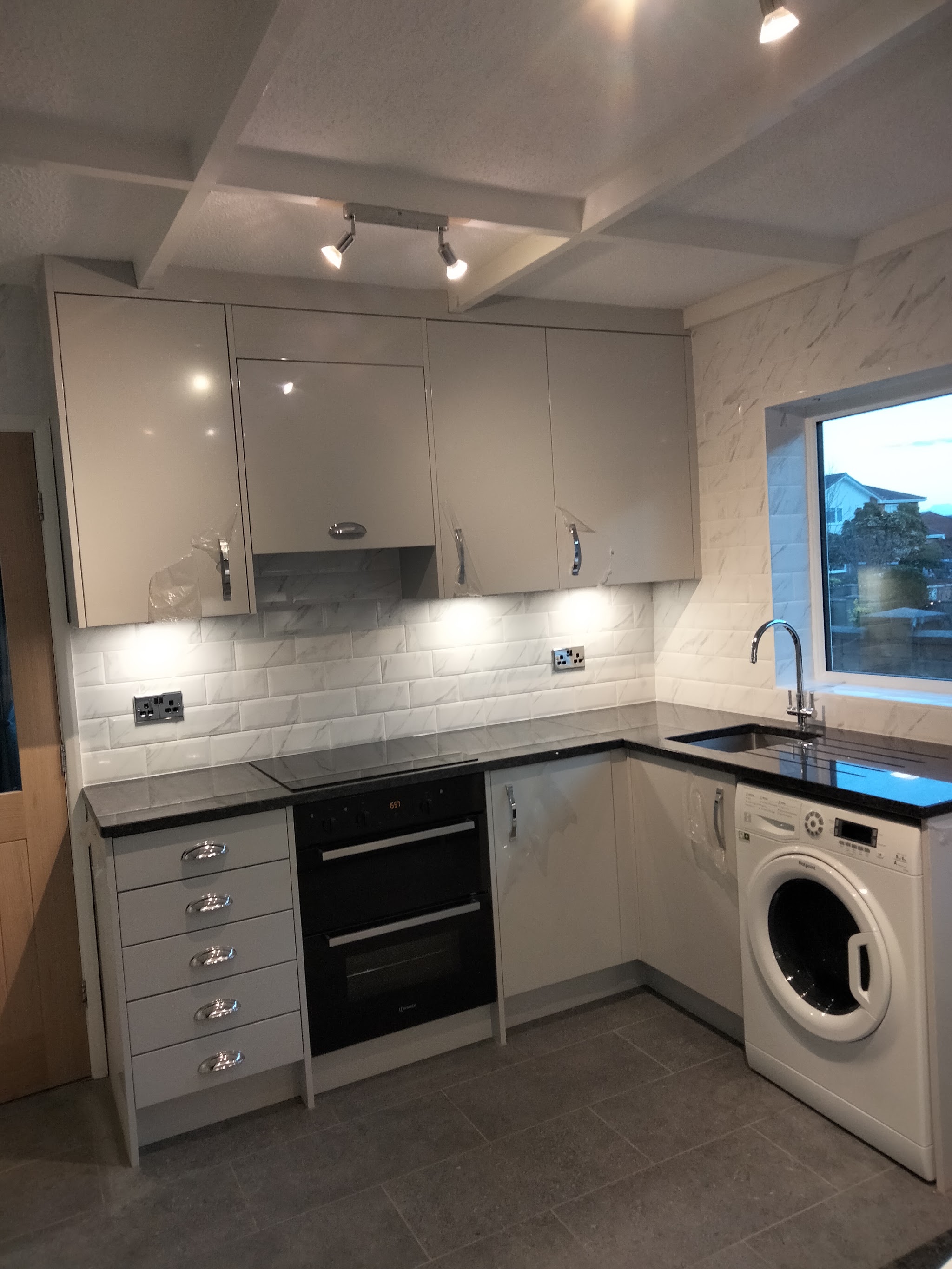 Light grey gloss kitchen units with dark granite worktops and white metro tiles
