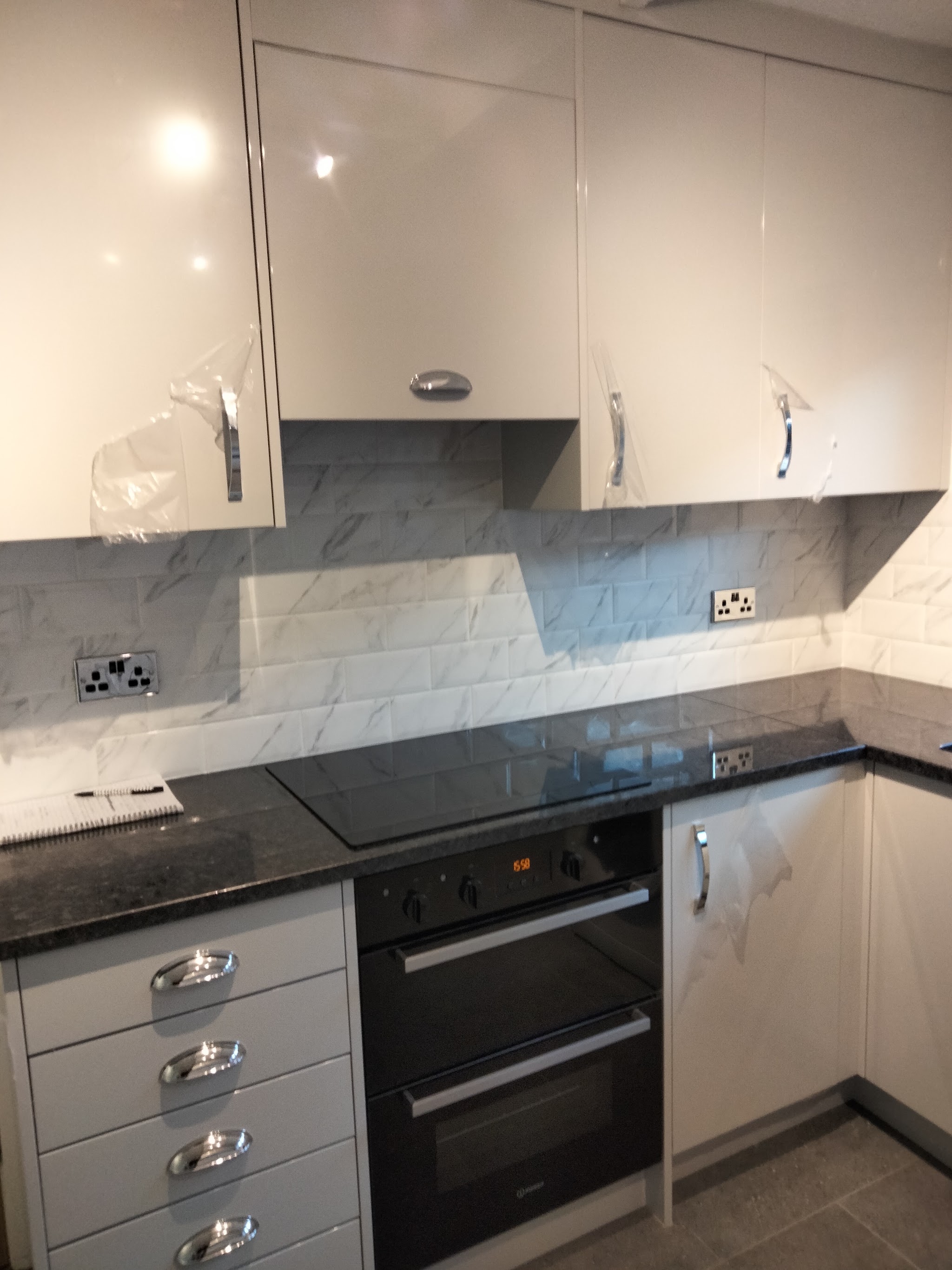 A double oven set into grey gloss units under a granite worktop