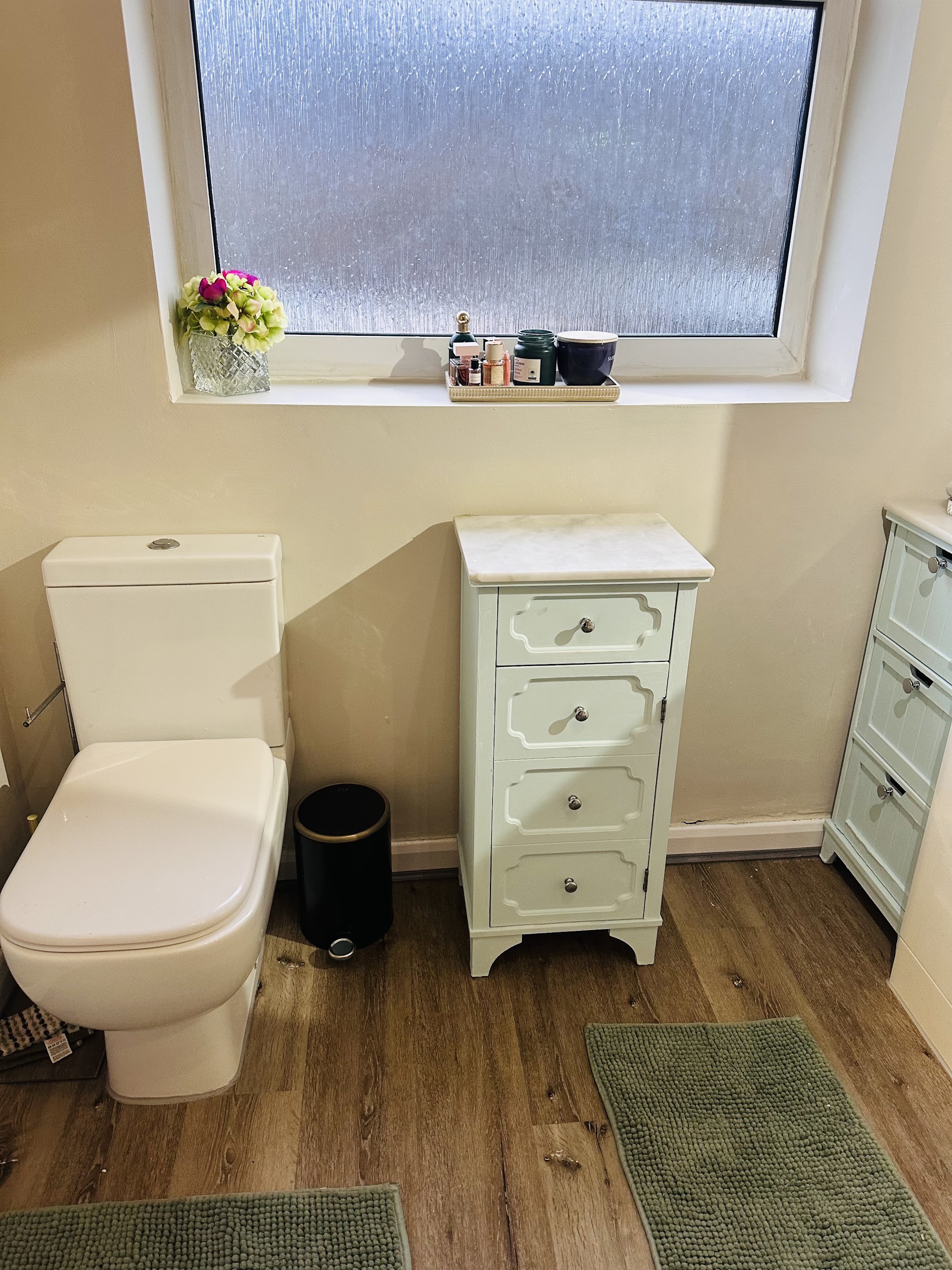 A close coupled toilet beside a white drawer unit on wood effect flooring